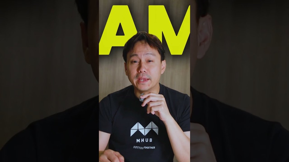 A presenter in a black MHub t-shirt talking to camera, with a large yellow caption above his head.